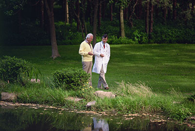 senior and doctor walking along side a pond